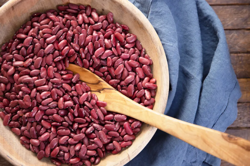 kidney beans on a wooden bowl with a wooden spoon on top of a blue clothing