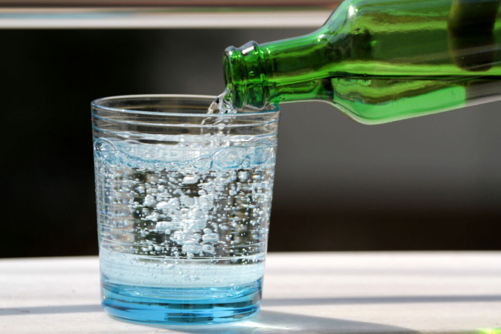 pouring a sparkling water from a green bottle to a glass