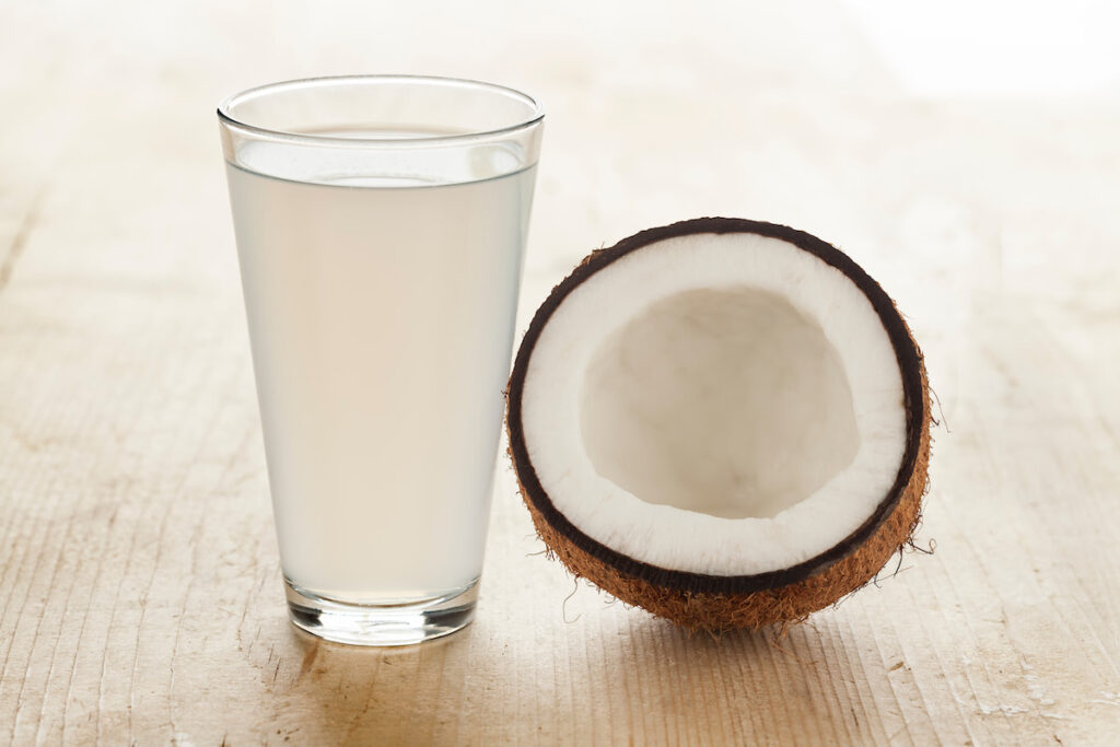 a glass of coconut water beside a coconut fruit