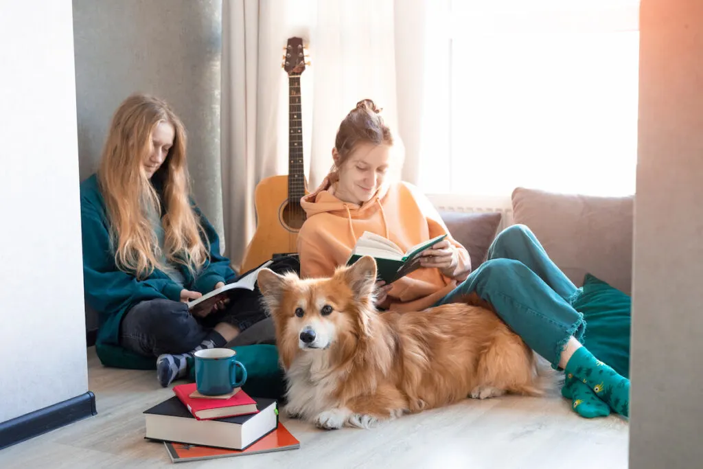 corgi laying on the floor while two young girls owner reading books