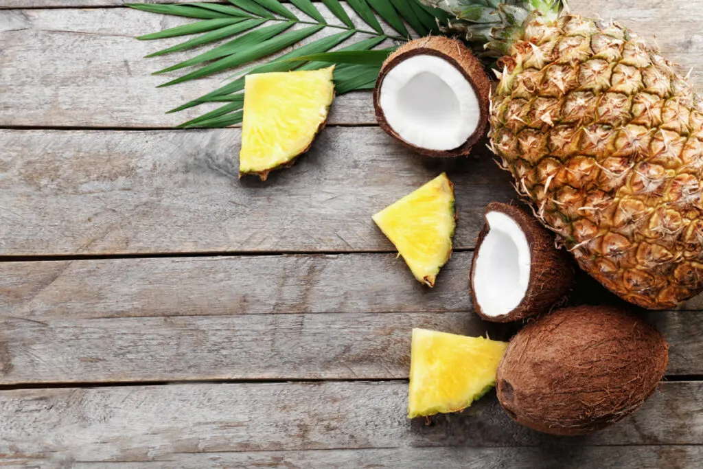 sliced pineapple beside a whole coconut and pineapple fruit on top of a wooden table