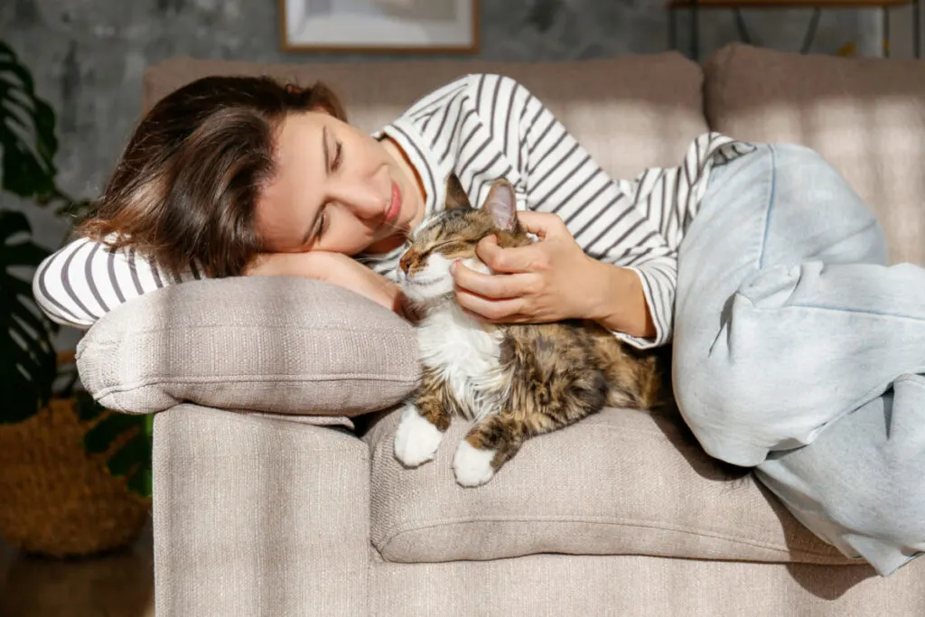 woman lying down on the sofa cuddling with her cat