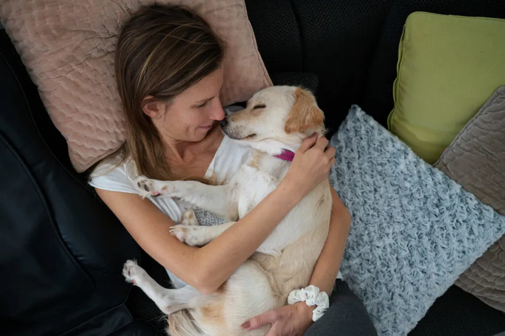 woman lying on bed cuddling her sleeping dog on top of her