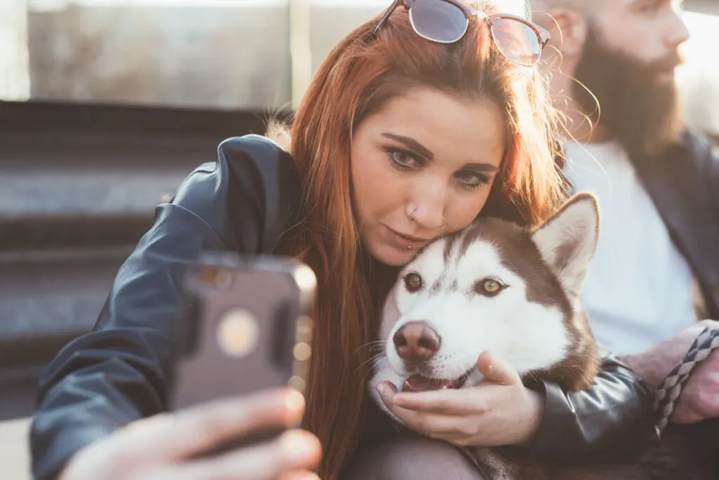 young woman with long hair taking selfie with her Siberian husky dog
