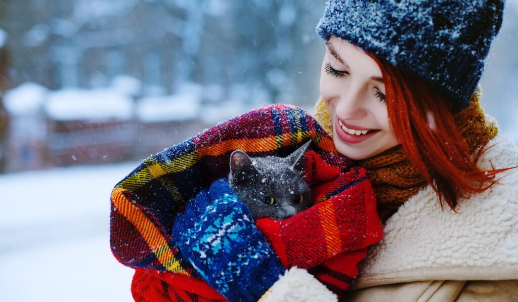 smiling girl carrying her gray cat in blanket 