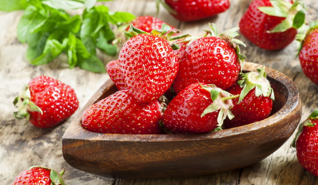 Fresh organic strawberries in a bowl in the shape of a heart, selective focus