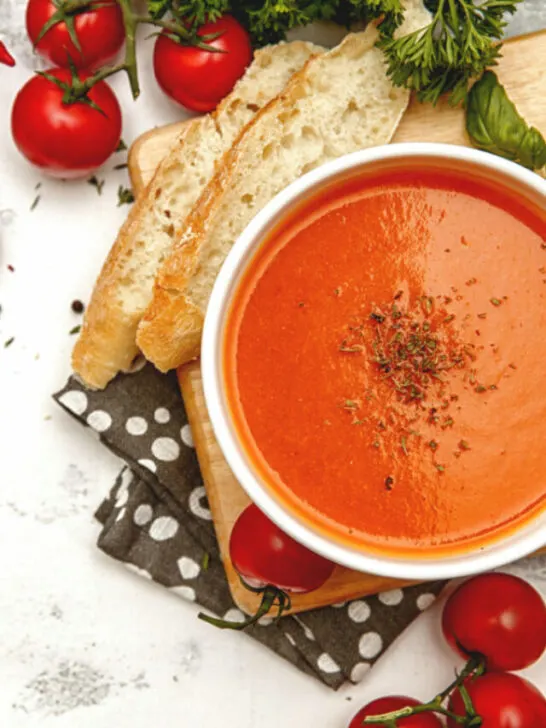 tomato soup in a white bowl white with ripe tomatoes at the side